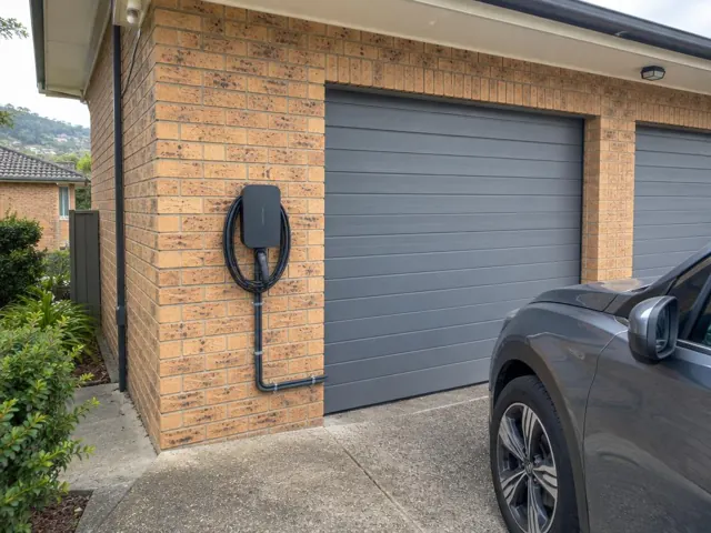 Wall-mounted EV charger on a brick exterior beside a garage door in Kotara