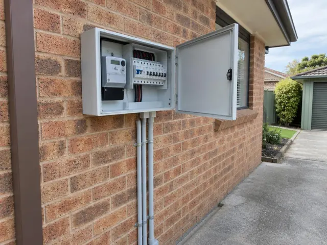 Outdoor electrical switchboard on a brick house wall with door open in Elermore Vale